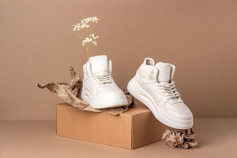 Eco leather shoes. A pair of beige sneakers with dry flowers on brown background. Casual sport lifestyle concept.