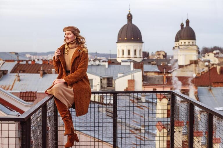 Outdoor full-length portrait of elegant fashionable happy smiling woman wearing trendy beige, brown outfit: beret, dress, faux fur coat, high suede boots, posing in European city. Copy, empty space Outdoor full-length portrait of elegant fashionable happy smiling woman wearing trendy beige, brown outfit: beret, dress, faux fur coat, high suede boots, posing in European city. Copy, empty space