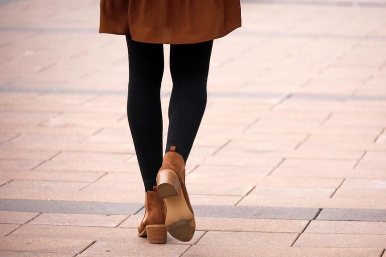Female legs in black warm tights and brown shoes. Slim girl walking on a street, fashion in autumn city Female legs in black warm tights and brown shoes. Slim girl walking on a street, fashion in autumn city
