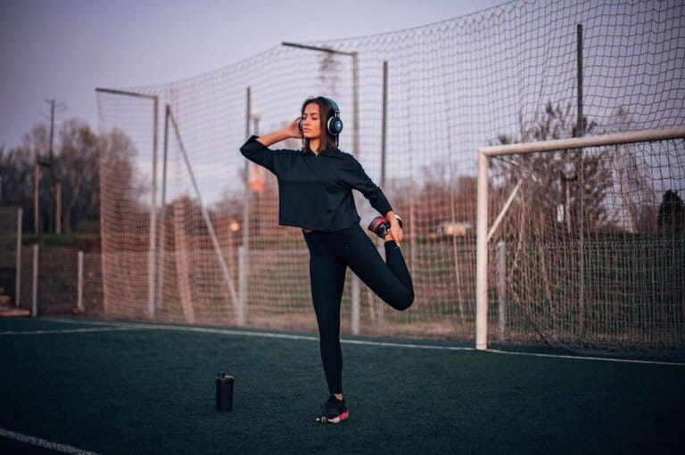 young girl with cropped hoodie with leggings, and sneakers is exercising on grass at sunset young girl with cropped hoodie with leggings, and sneakers is exercising on grass at sunset