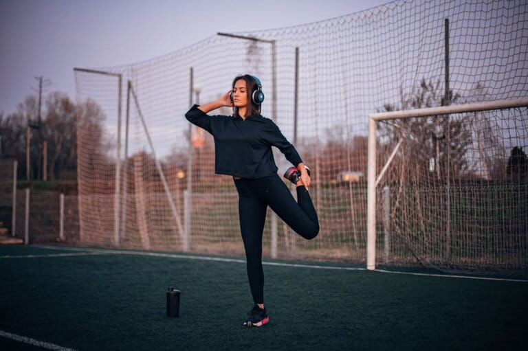 young girl with cropped hoodie with leggings, and sneakers is exercising on grass at sunset